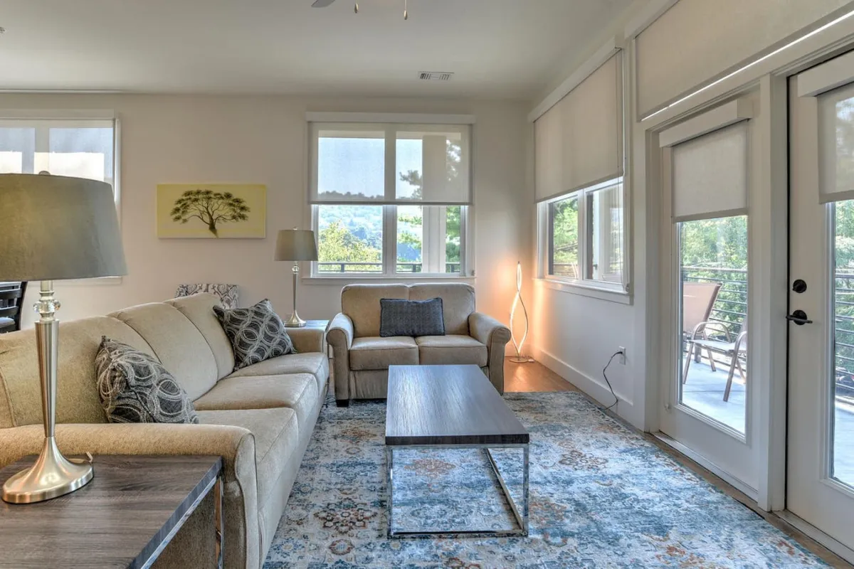 A comfortable living area with a sofa, coffee table, a lamp, and large windows letting in ample natural light. The windows become a focal point, offering a glimpse of the outside and suggesting a seamless transition from indoor relaxation to urban exploration.