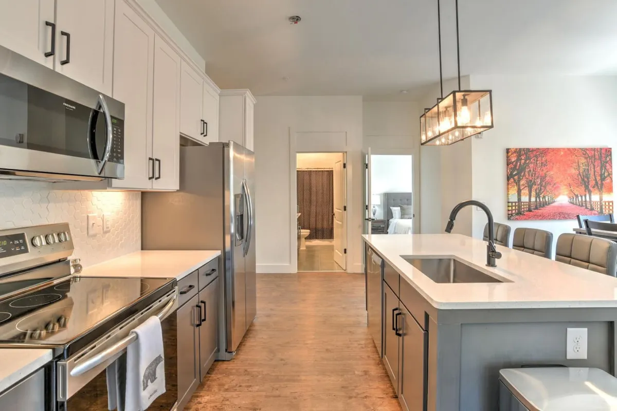 A modern kitchen and dining area with a kitchen island, stainless steel appliances, and inviting artwork. The setup is practical for quick meals before heading to meetings or for hosting casual gatherings, reflecting the convenience expected by business travelers.
