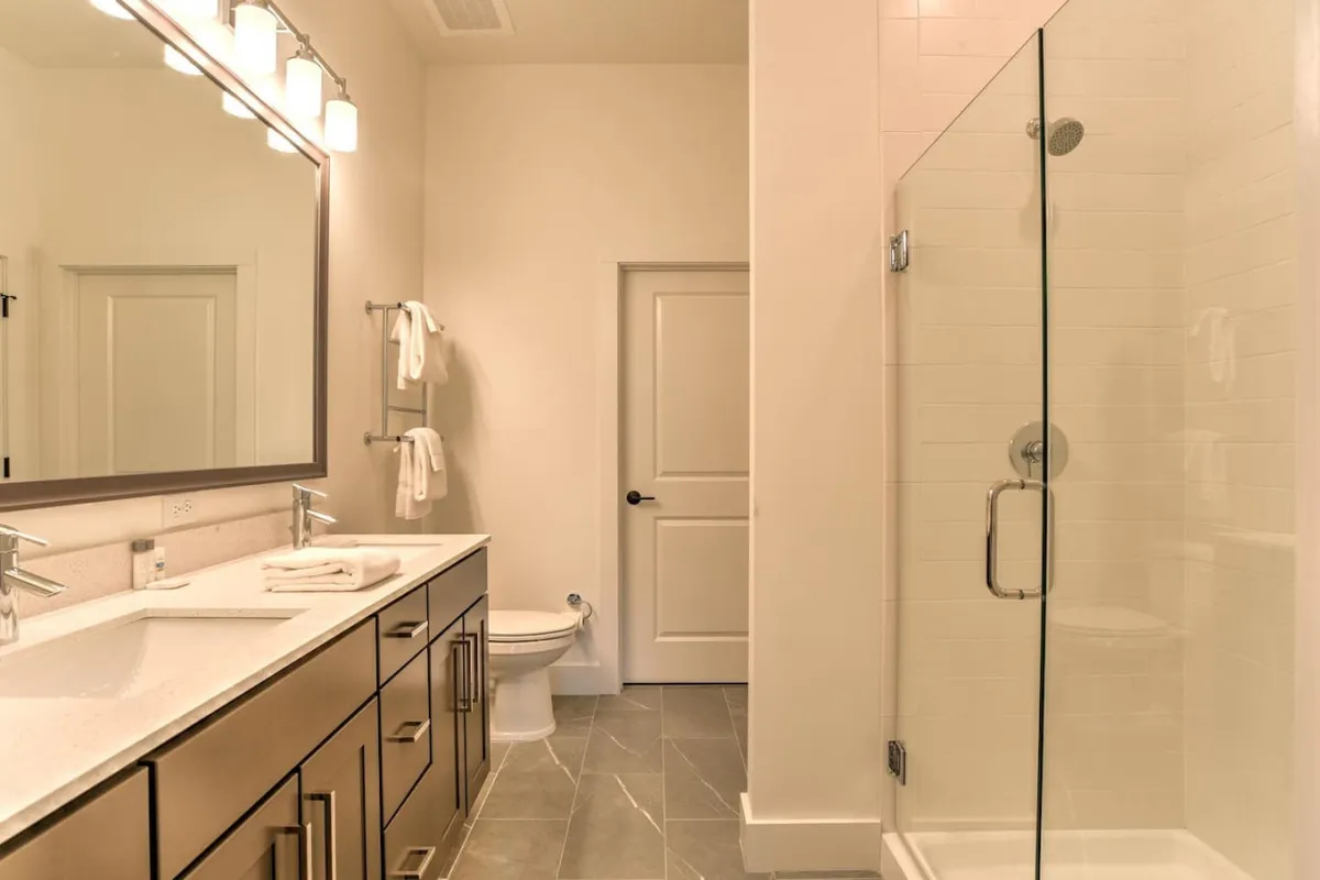 A fresh, well-appointed bathroom featuring double sinks, a large illuminated mirror, and a glass shower enclosure. The space suggests a spa-like atmosphere, ideal for unwinding and rejuvenating.