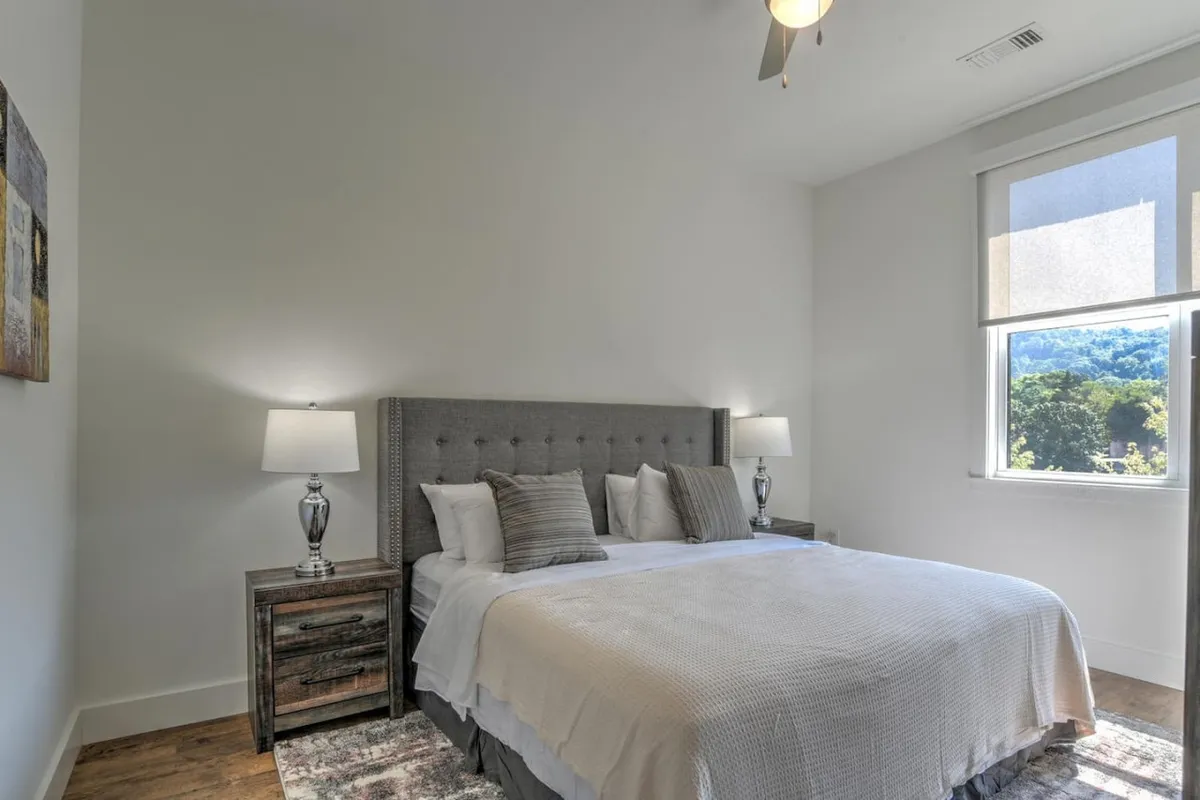 A serene bedroom featuring a king-size bed adorned with crisp linens, nightstands, tasteful artwork, and a window offering a view of the outdoors. The space is bathed in soft natural light, radiating calm and comfort.