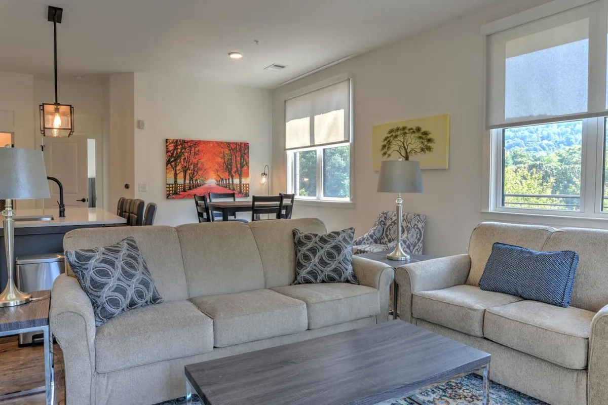 A bright, art-filled living space with a plush sofa, elegant dining table, and large windows. The scene feels cozy yet spacious, ideal for socializing or enjoying a quiet moment before heading out to Asheville’s attractions.