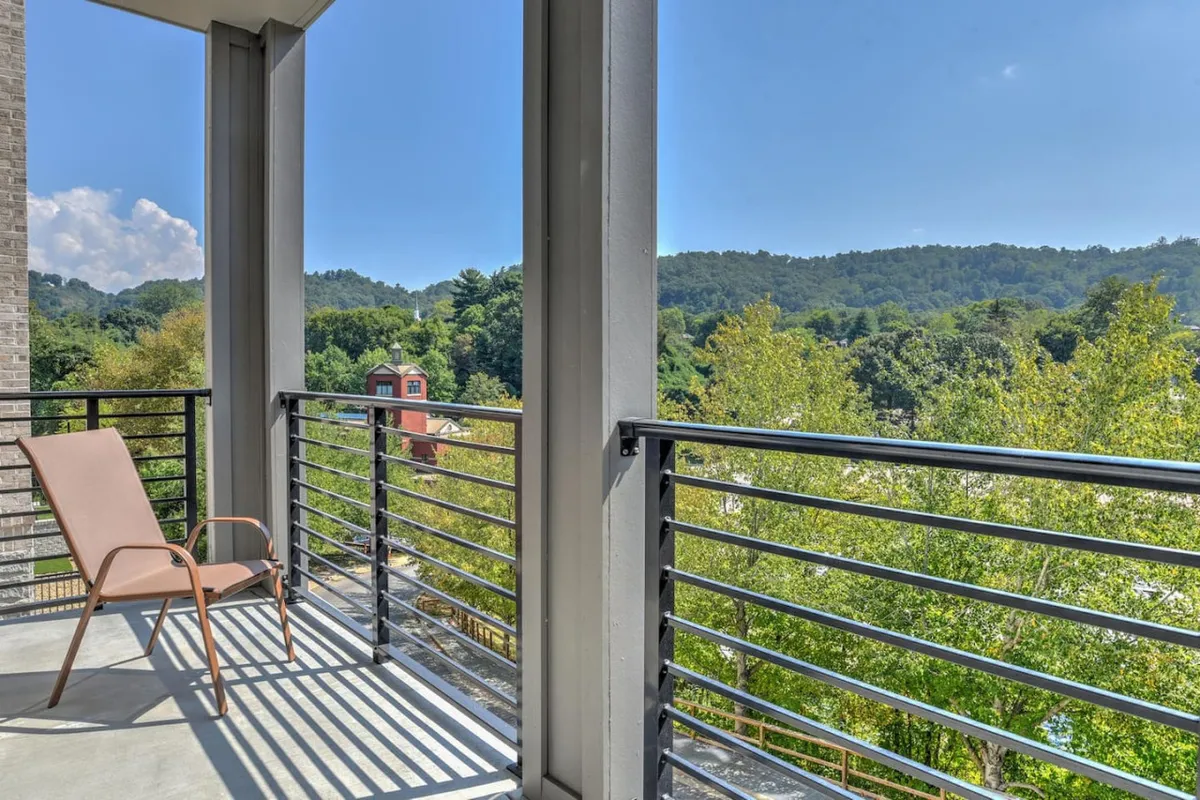 A serene balcony scene featuring a lounge chair positioned to face the mountain horizon, framed by a modern balcony railing. The setting showcases the outdoor seating, inviting guests to relax, read, or enjoy a cup of tea while taking in the natural beauty. The soft morning light and open air evoke a tranquil mood, with a clear view of the mountains in the distance.
