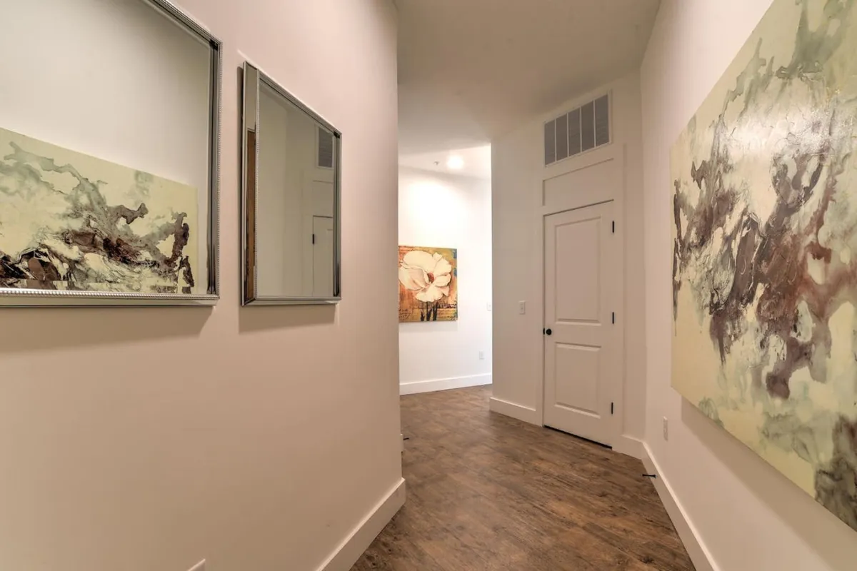 A calm and well-lit hallway with abstract wall art and a doorway leading to another room. Mirrors enhance the sense of space and tranquility, suggesting a smooth and inviting transition upon entering the condo.
