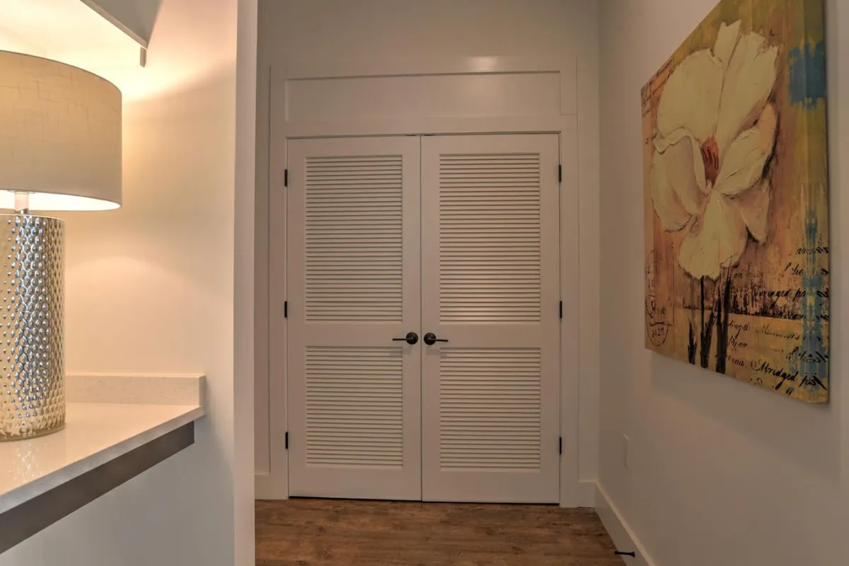 An inviting entryway featuring double doors, a lamp providing warm lighting, and a flower painting on the wall. The space is styled to make a positive first impression, with a hint of the home's interior design visible beyond the doors.