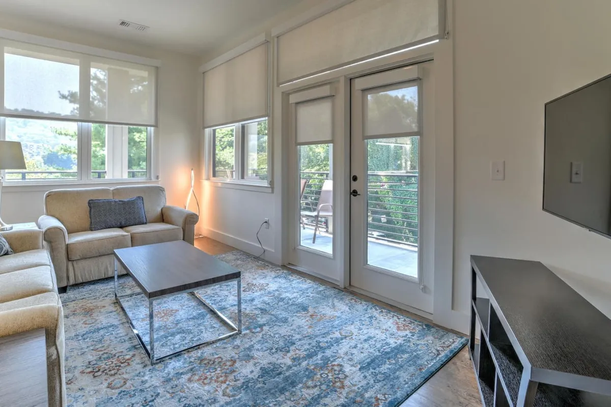 A spacious living area with a comfortable sofa (ideal for a sofa bed), coffee table, large windows with balcony doors, and abundant natural light. The scene invites guests to relax, socialize, or unwind after a day out.