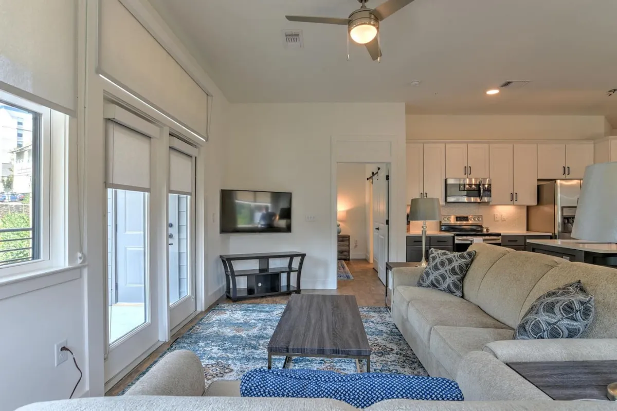 This image captures a stylish open-concept living area, featuring a modern sofa, coffee table, television, and an inviting kitchen space in the background. The abundance of natural light and cozy decor suggest a comfortable spot for relaxing or entertaining after a day exploring the city.