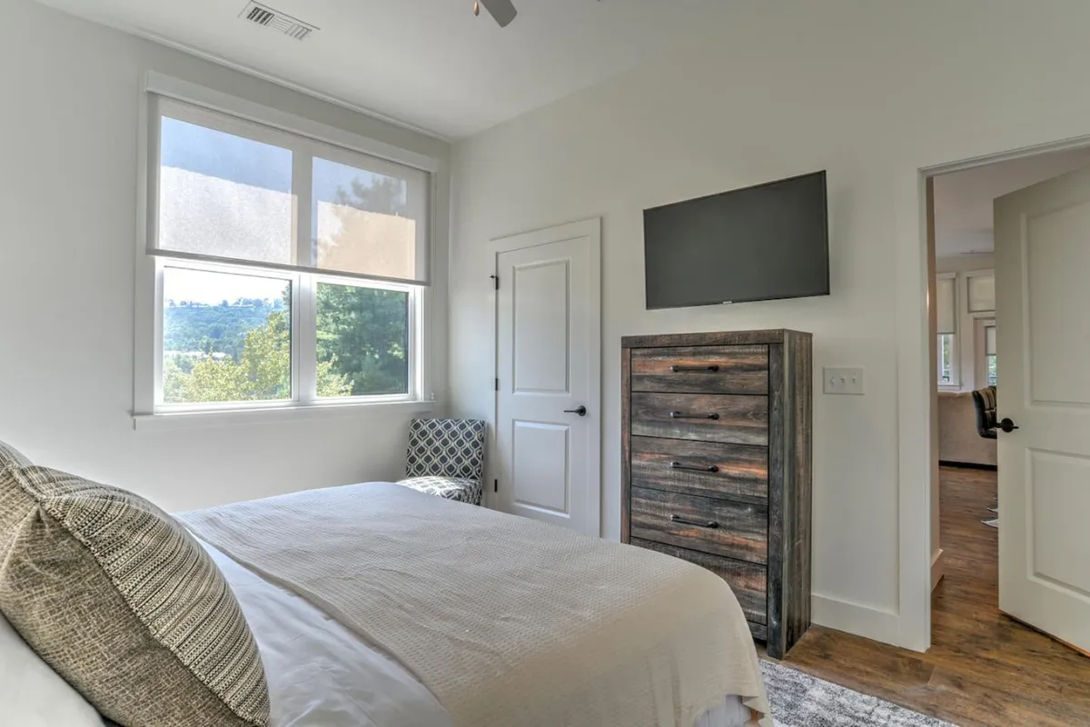 A tranquil bedroom with a plush bed, cozy armchair by the window, dresser, and soft lighting. The inviting atmosphere suggests a comfortable space for relaxation, reading, or enjoying a morning coffee.